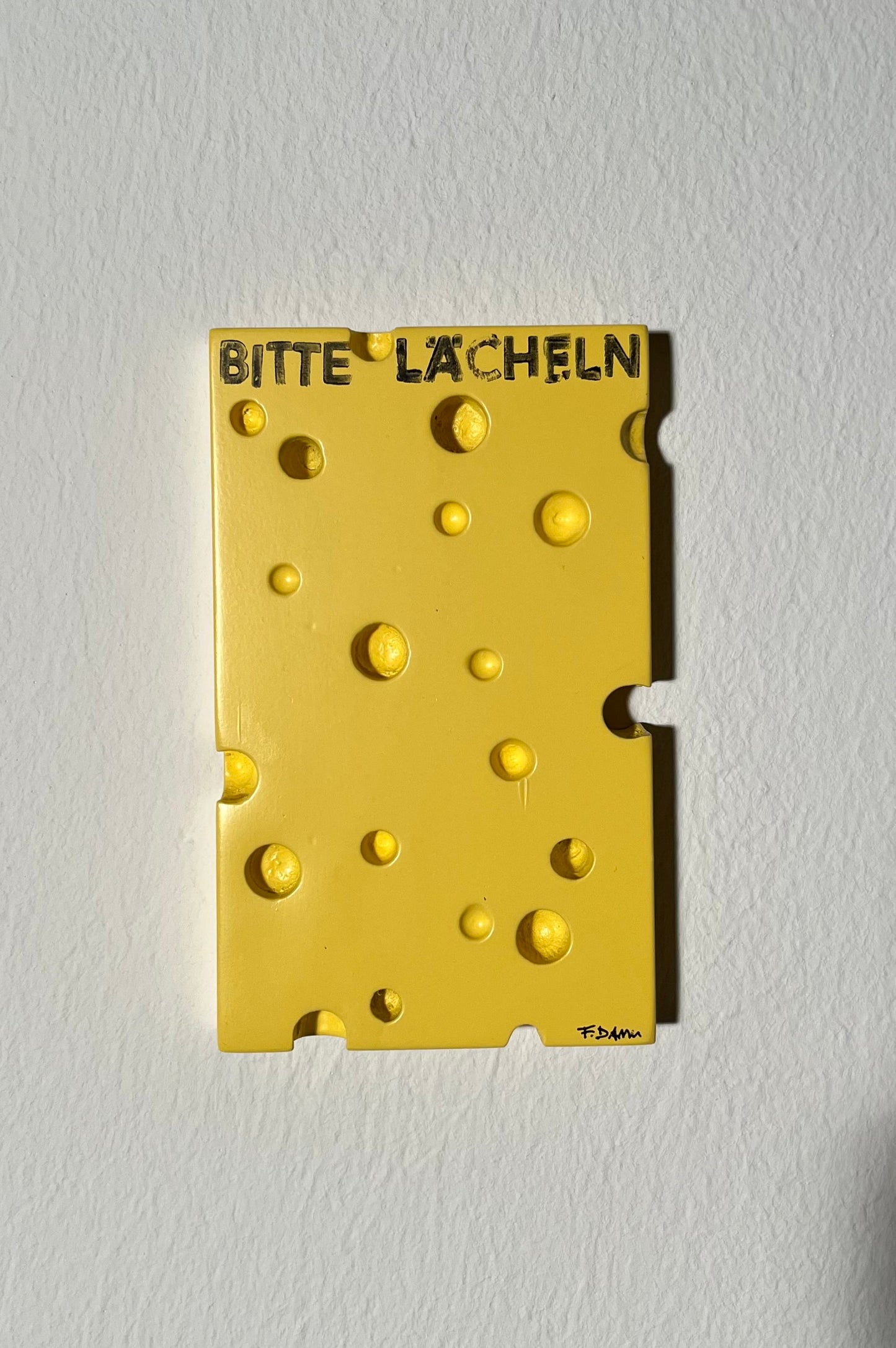 Yellow cheese-shaped object with 'BITTE LACHEN!' text on a white background