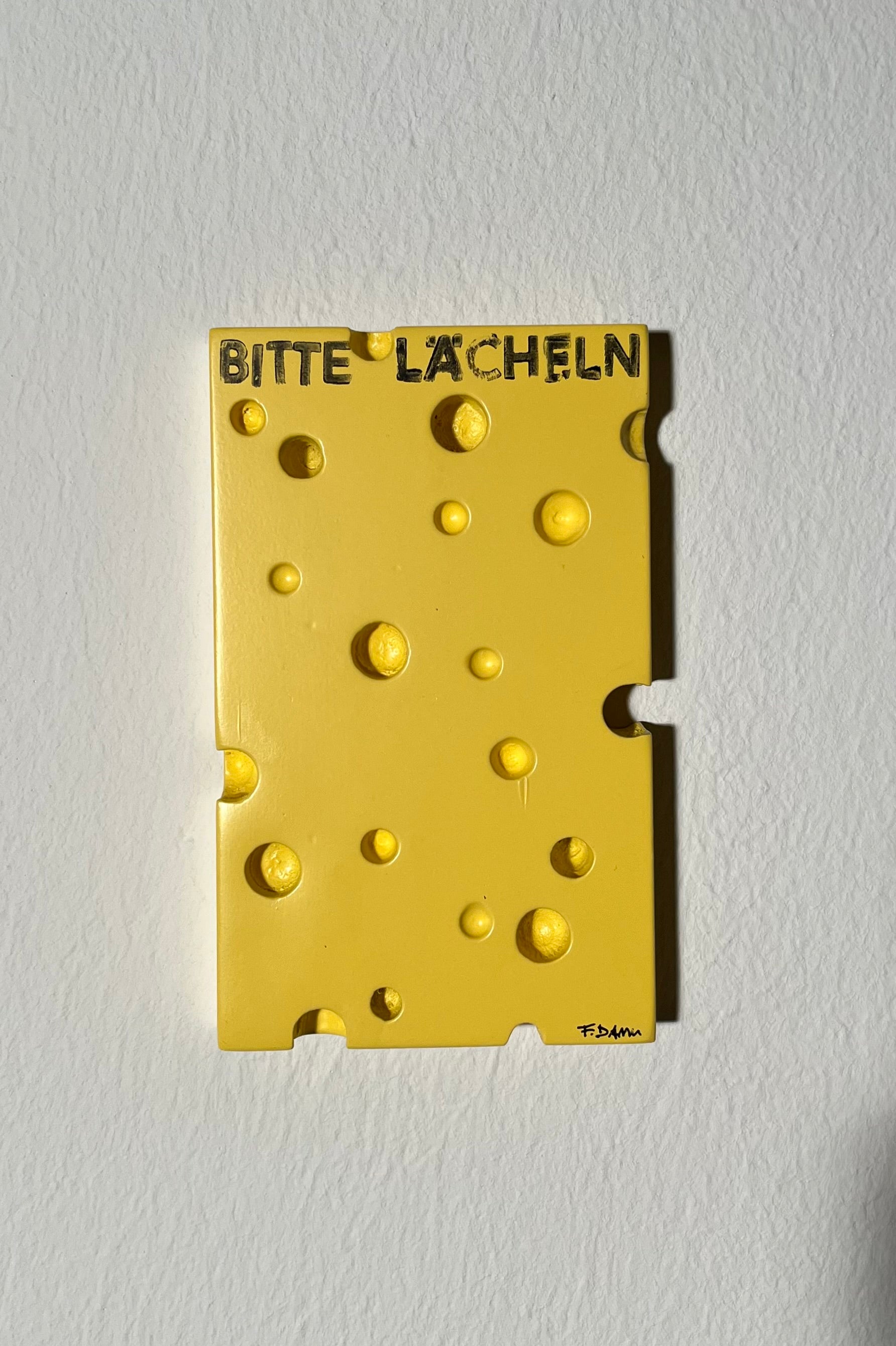 Yellow cheese-shaped object with 'BITTE LACHEN!' text on a white background